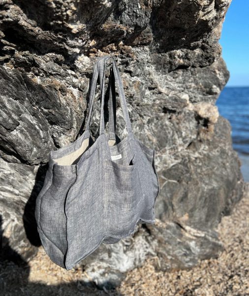 graue Strandtasche von Linen Couture aus Leinen, Ökotex, an Fels hängend, im Hintergrund Meer